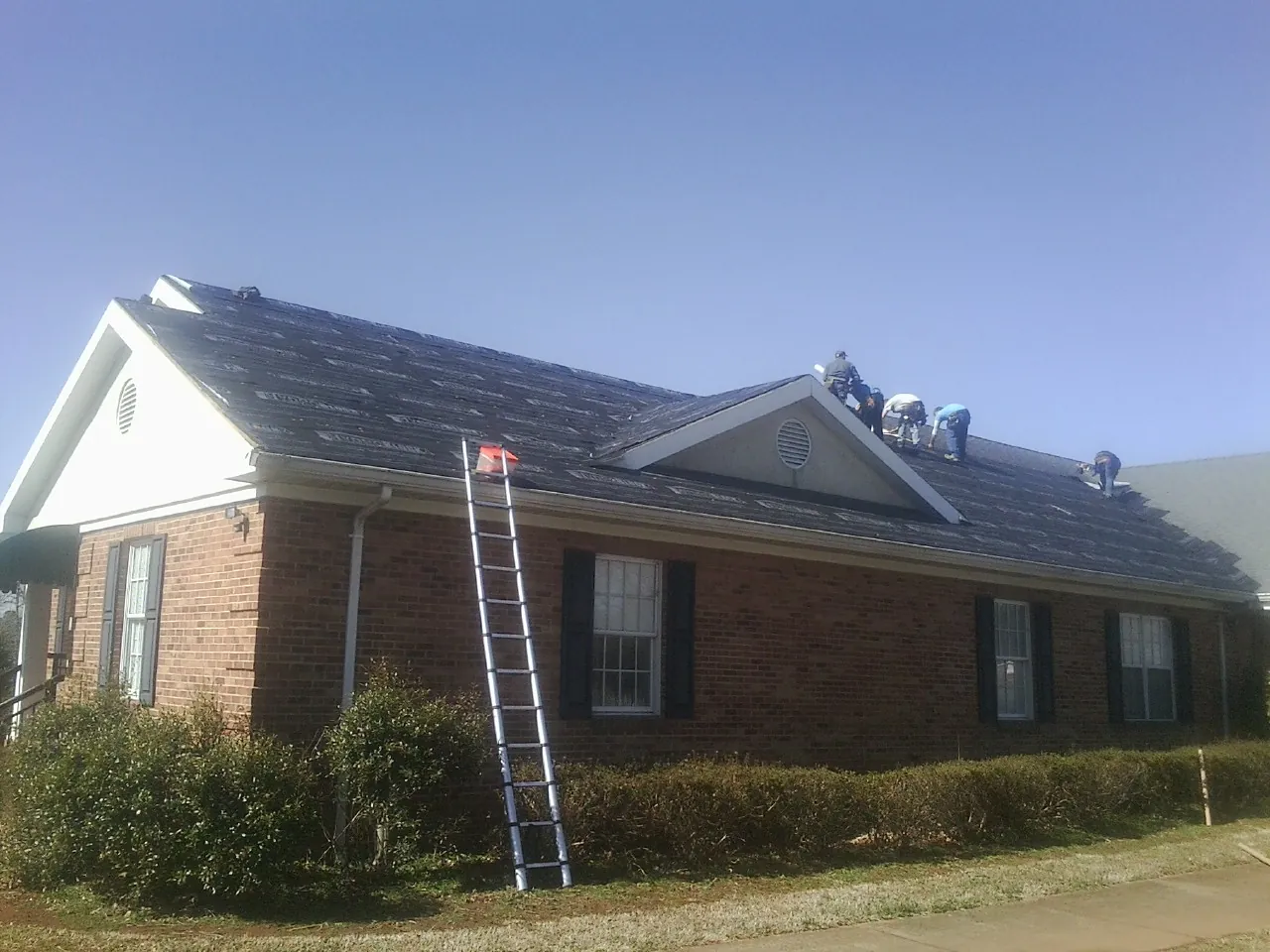 Crew tearing shingles off a brick ranch roof with a ladder set — Metal Roof Repair work by our crew in Toledo